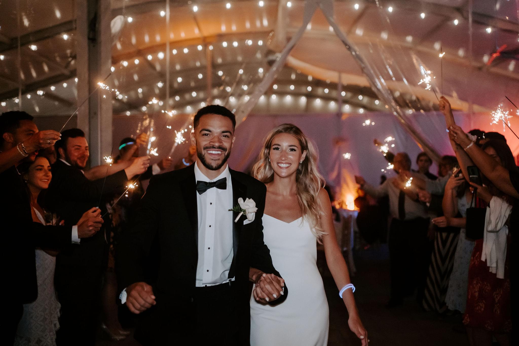 Wedding couple walking into their wedding reception and guest standing and cheering them on.