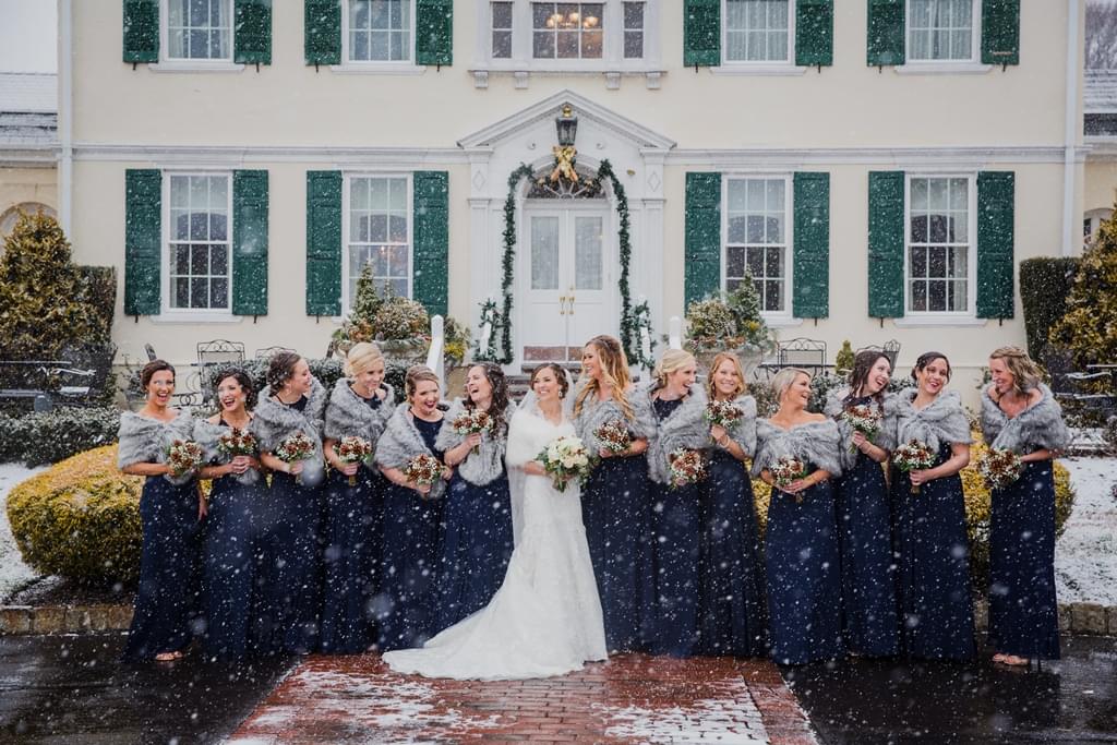 Bride with her bridesmaids posing for a winter wedding photoshoot in the snow at Pen Ryn Estate.